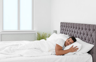 Young man sleeping in bed with soft pillows at home