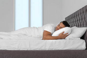Young man sleeping in bed with soft pillows at home