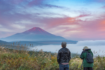 Fototapeta premium two men admired and shooting photo at mountain Fuji without snowcap in a summer morning with dramatic red clouds blue sky and mist below.
