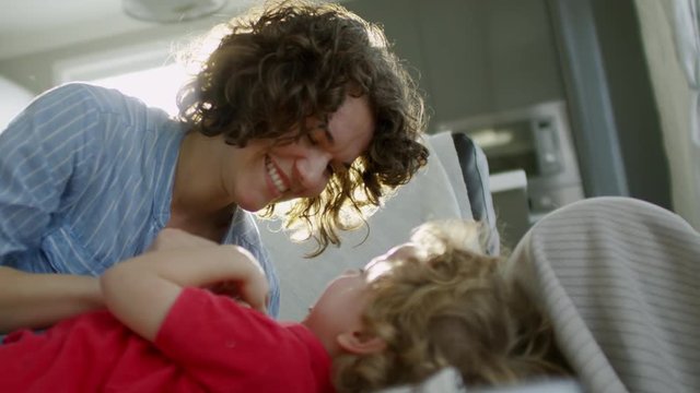 Medium shot of loving mother cuddling with little son of preschool age when having fun together at home