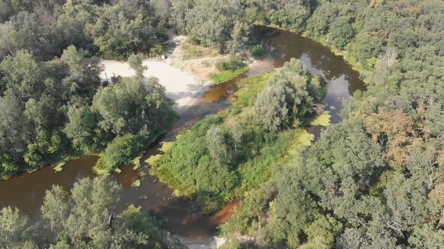 The river bed is a top view from the drone. The quadrocopter is flying over the river in the forest. Nature, green vegetation on the banks of the river. green reeds and trees. Small pond,flows. Summer