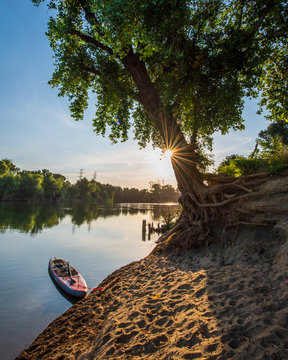 Sunrise On A Calm River With A Paddleboard In The Foreground