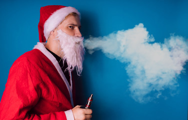 Guy dressed as Santa Claus vaping electronic cigarette with smoke on blue background closeup. Man...
