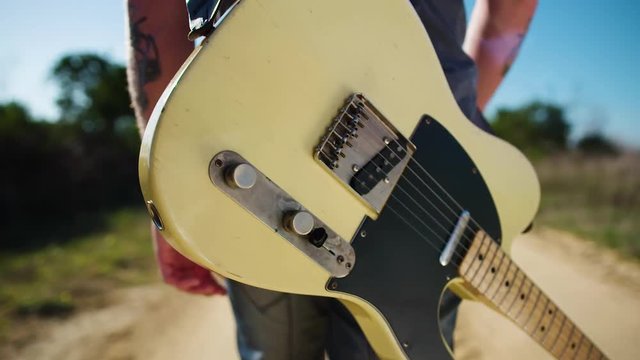 Closeup of musician walking down dusty track with guitar.
