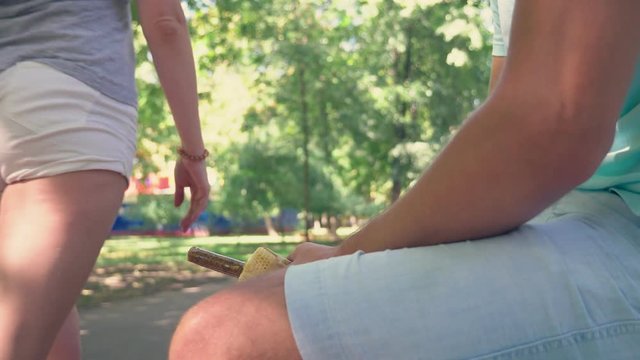 a young lonely guy holding a hotdog, in the lower abdomen, sitting on a bench in the park, and open the hotdog packaging, imitating an erection . 4k, slow-motion