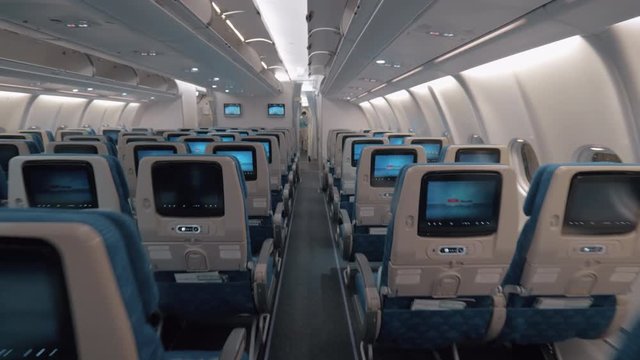 Steadicam shot of walking through the empty economy class in the airplane. Rows of seats with working seat monitors