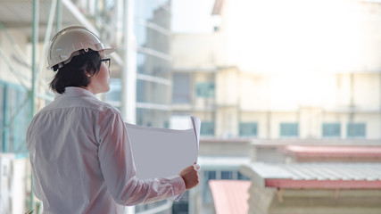 Engineer or Architect checking architectural drawing while wearing a personal protective equipment safety helmet at construction site. Engineering, Architecture and construction business concepts