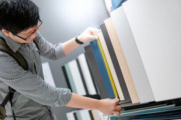 Asian man using tape measure on cabinet panel choosing materials or countertops for built-in...