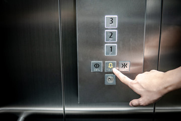 Male forefinger pressing on emergency stop and alarm button in elevator (lift). Mechanical...
