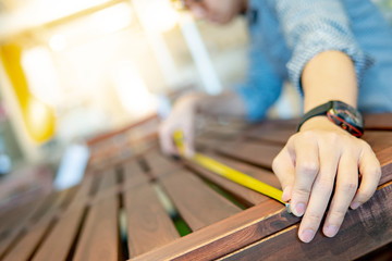 Young Asian man using tape measure for measuring wooden outdoor table in showroom. Shopping...