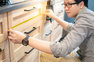 Young Asian man using tape measure for measuring modern kitchen counter in showroom. Shopping furniture for home improvement concept
