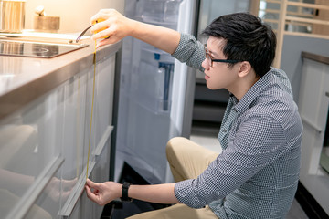 Fototapeta na wymiar Asian man using tape measure on kitchen counter