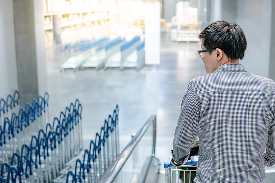 Young Asian man shopper holding shopping cart (trolley) on travelator (escalator) in supermarket or grocery store. Shopping lifestyle concept