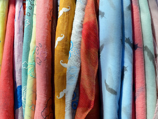 A lot of light scarfs of different colors (red, yellow, orange, blue, green) on a hanger close up