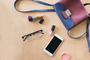 Fashion concept : Flat lay of red leather woman bag open out with cosmetics, accessories and smartphone on wedden background.