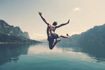 Fotobehang Man jumping with joy by a lake © Rawpixel.com