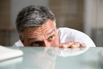 Frightened Businessman Peeking From The Edge Of Desk