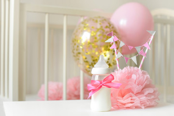 Baby bottles with breast milk with various festive paper decor and balloons in front of baby bedroom. It's a girl or baby birthday celebration concept. Baby shower concept.