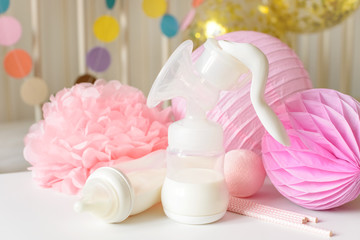 Breast pump and baby bottles with milk, various festive paper decor and balloons in front of baby bedroom. It's a girl or baby birthday celebration concept. Baby shower concept.