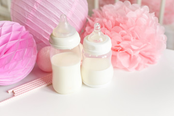 Obraz na płótnie Canvas Baby bottles with breast milk with various festive paper decor and balloons in front of baby bedroom. It's a girl or baby birthday celebration concept. Baby shower concept.