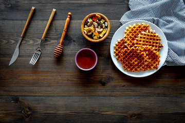 Traditional belgian waffles with dried fruit, nuts and caramel on dark wooden background flat lay copy space