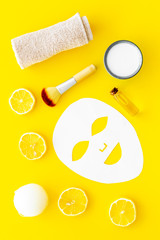 Fototapeta na wymiar Face spa products. Facial mask, cream, oil near lemon slices and towel on yellow background top view