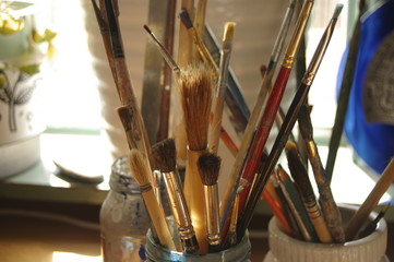 glass jar of well used varying artist's paint brushes drying in the artist's studio
