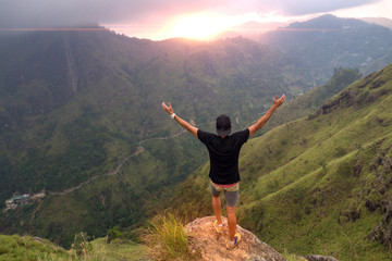 Hiker standing on top of a mountain with raised hands and enjoying sunrise