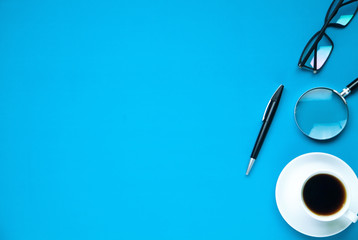 Coffee cup, pen, magnifier and glasses on a blue background.