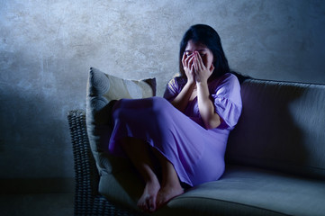young sad and depressed Asian Chinese woman at home sofa couch crying desperate and helpless...