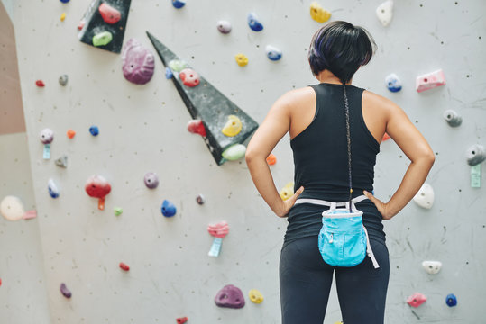 Rear view of sportswoman with sack of powdered chalk on her waist looking at bouldering wall