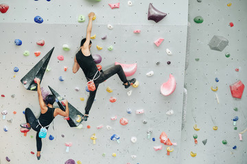 Couple practicing rock climbing on artificial wall indoors - obrazy, fototapety, plakaty
