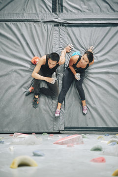 Vietnamese young people resting on mat and drinking water after bouldering