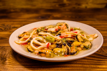 Ceramic plate with different sea food and olives on wooden table