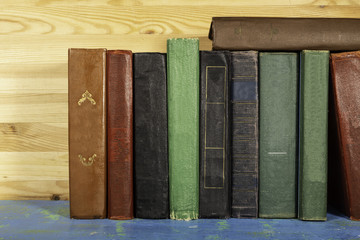 a stack of old books standing side by side on a shelf, wooden background.