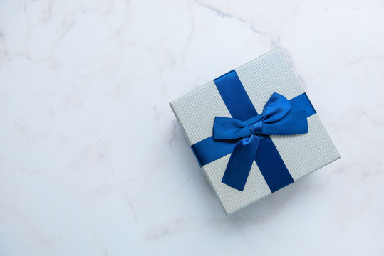Gift box with blue ribbon on white marble background, top view. Gifts,  celebration, valentines theme Stock Photo