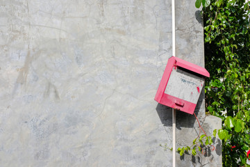 Red steel mailbox with pale sticker mention 'cars, motorcycle, if the your asset are stolen...' on concrete wall and green vine