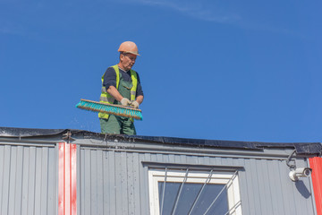 Worker at the construction site cleans the roof of the water with a brush