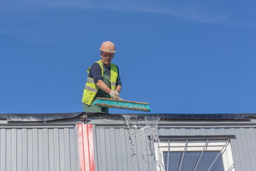 Worker at the construction site cleans the roof of the water with a brush