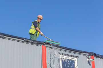 Worker at the construction site cleans the roof of the water with a brush