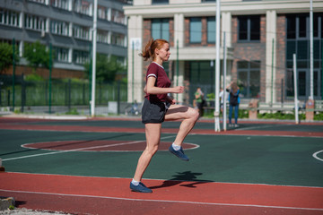 Red-haired young girl runs in the stadium. Student delivers standards for running outdoors. Young...