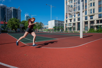 Fototapeta premium Red-haired young girl runs in the stadium. Student delivers standards for running outdoors. Young woman running on the football field