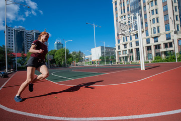 Red-haired young girl runs in the stadium. Student delivers standards for running outdoors. Young...