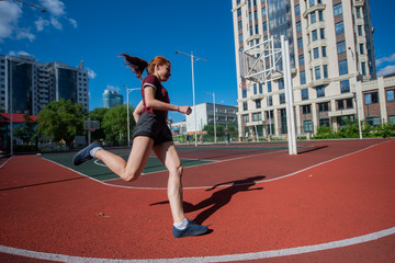 Red-haired young girl runs in the stadium. Student delivers standards for running outdoors. Young woman running on the football field