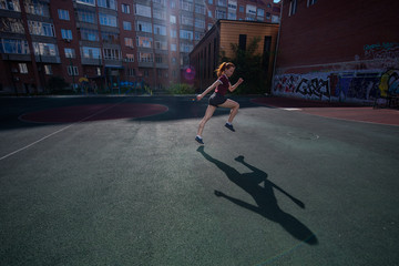 Red-haired young girl runs in the stadium. Student delivers standards for running outdoors. Young...