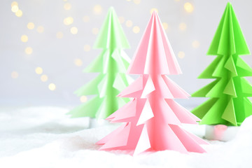 Origami 3D Xmas tree from paper on white background and bokeh lights. Merry Christmas and New Year card. Paper art style. Copy space. Selective focus