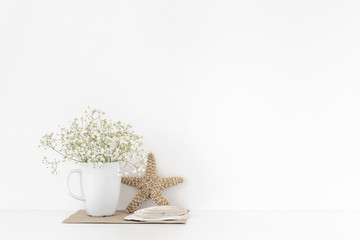 Background with stationary, seashells, sea star, bouquet of white flowers in mug on white wall...