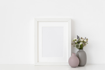 White a5 portrait frame mockup with dried field wild flowers and vases on white wall background. Empty frame, poster mock up for presentation design. Template frame for text, lettering, modern art.