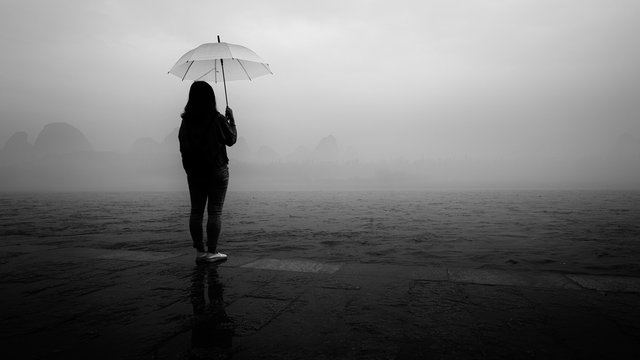 Girl holding umbrella by the river on a foggy morning