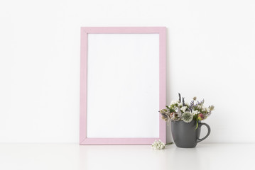 Pink a4 portrait frame mockup with dried field wild flowers in gray mug on white wall background. Empty frame, poster mock up for presentation design. Template frame for text, lettering, modern art.